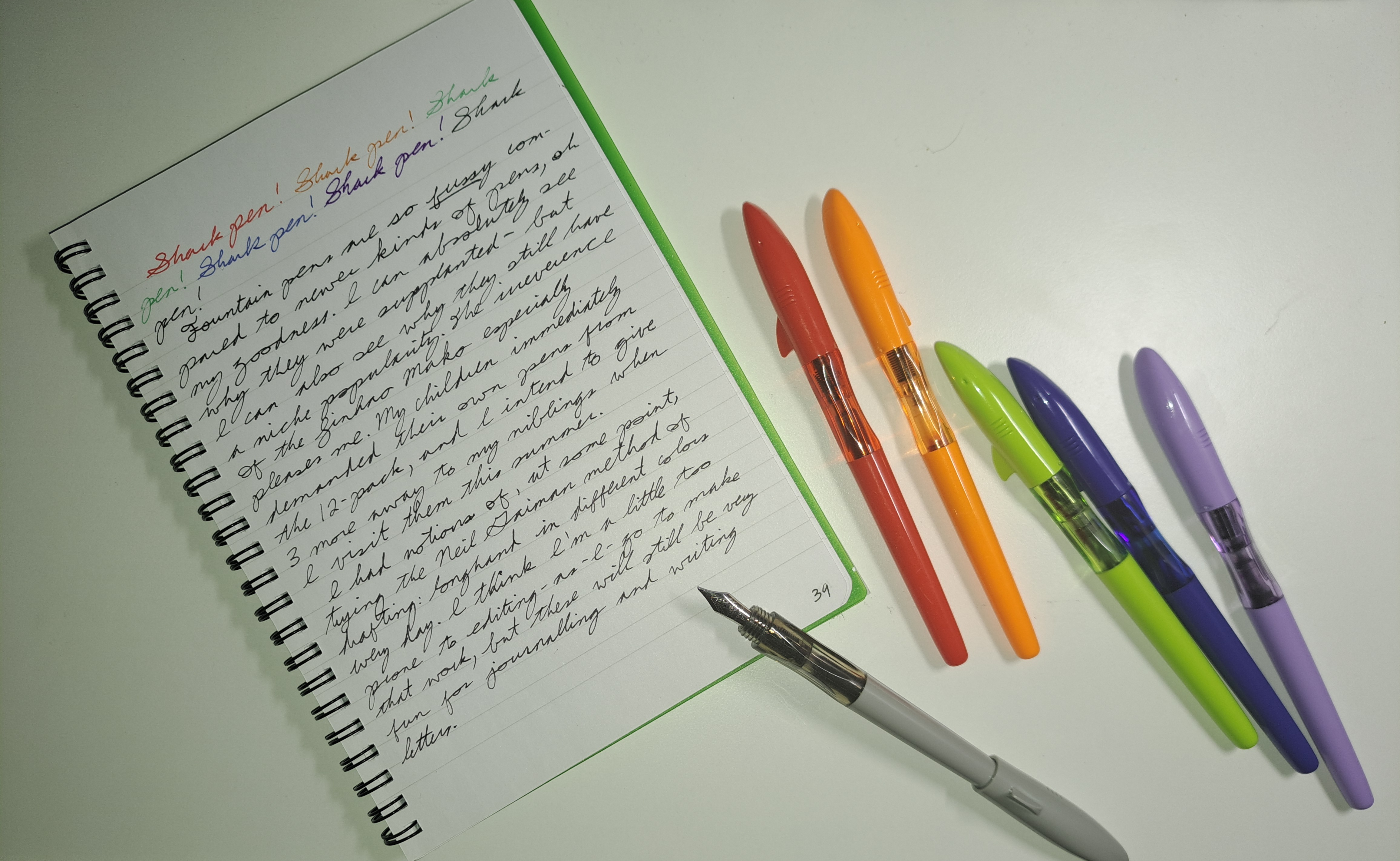 shark pens multicoloured fountain pens with shark head lids, and a page of cursive writing in different colours